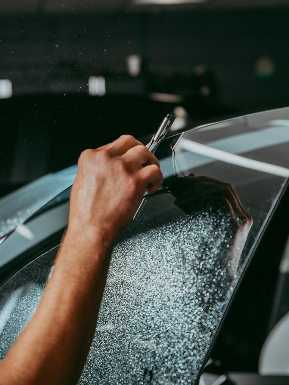 A person is applying tinted glass to a car windshield.