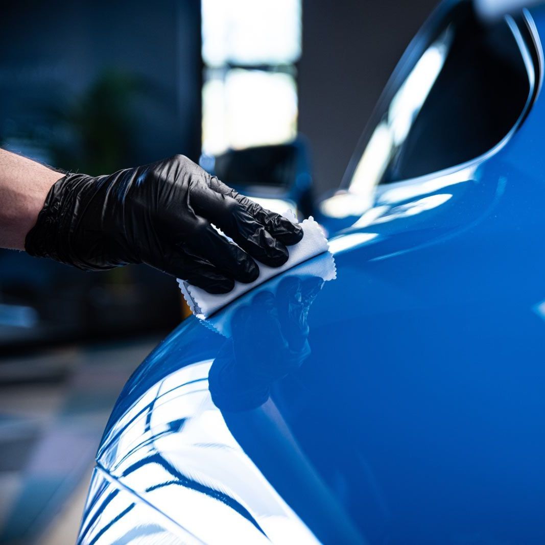 A person is cleaning a blue car with an orange towel