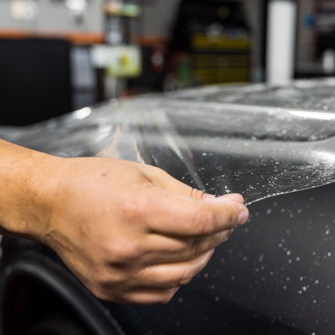A person is cleaning a blue car with an orange towel