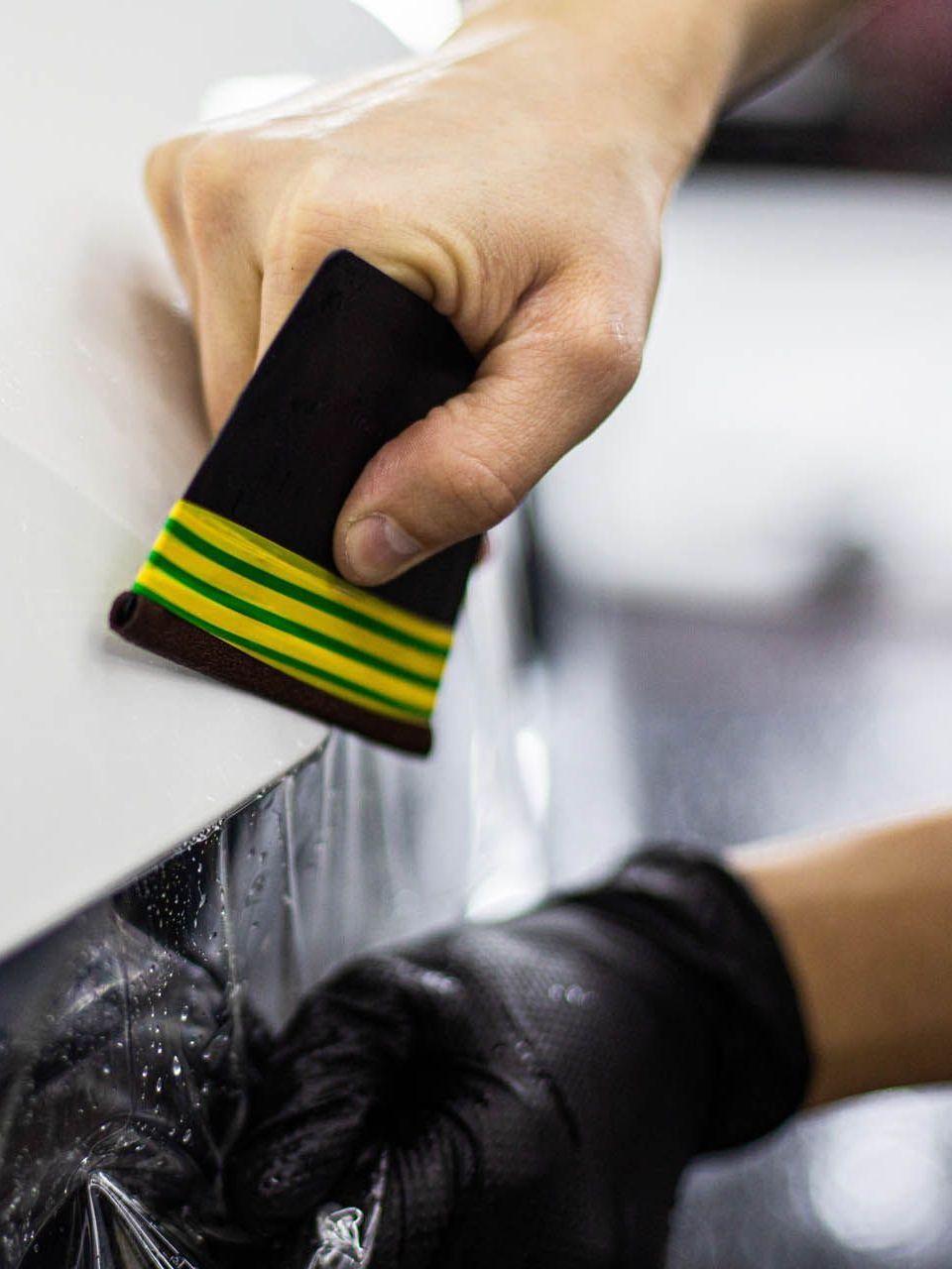 A person is applying a clear film to the hood of a car.
