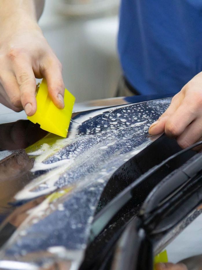 A person is cleaning a blue car with an orange towel