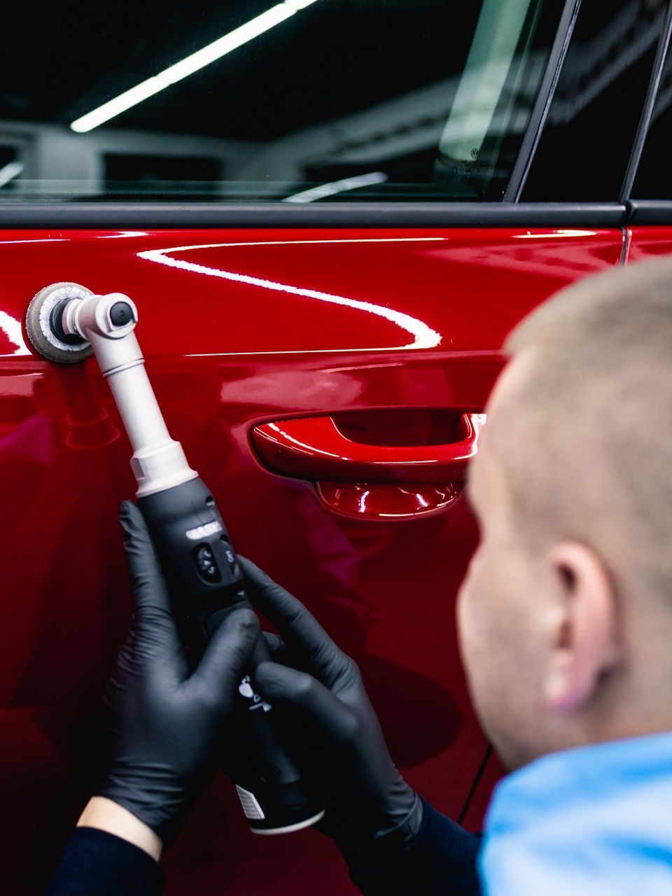 A man is polishing a red car with a machine.