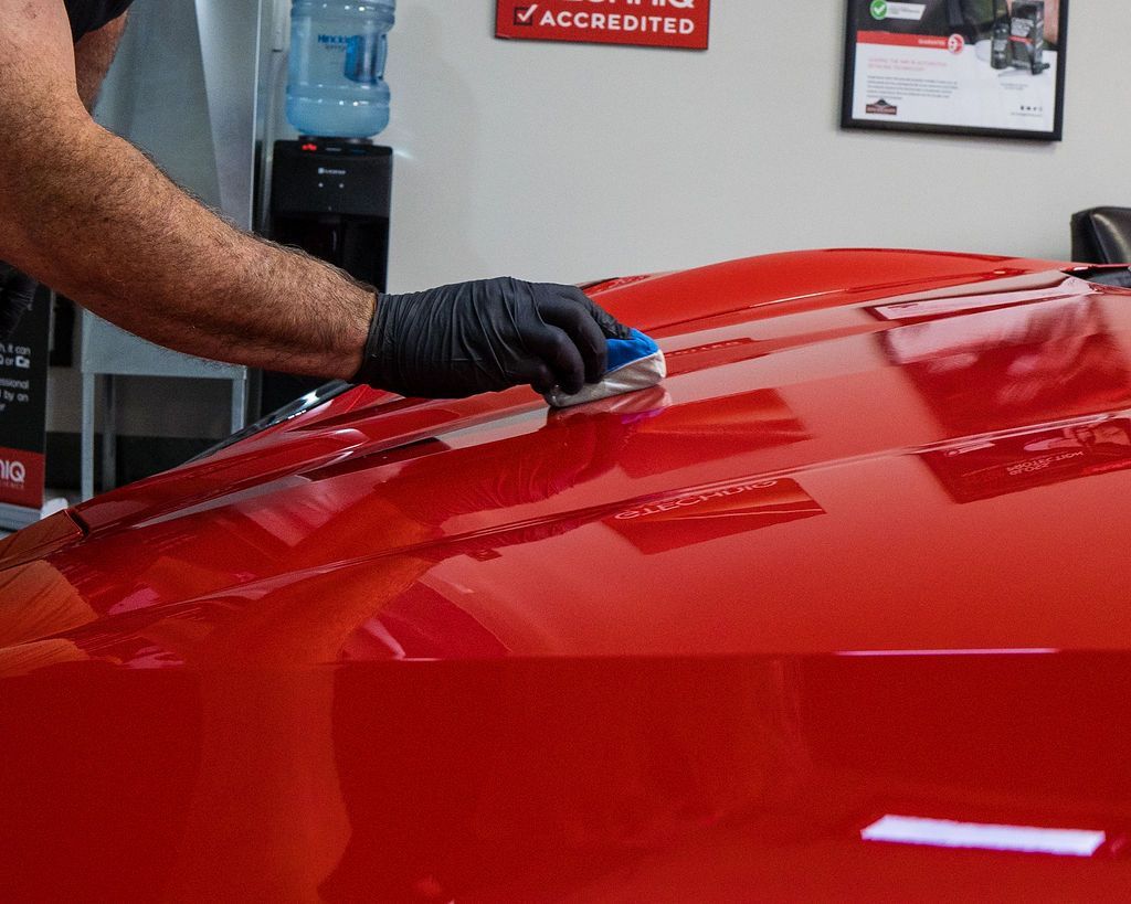 A man is polishing the hood of a red car.