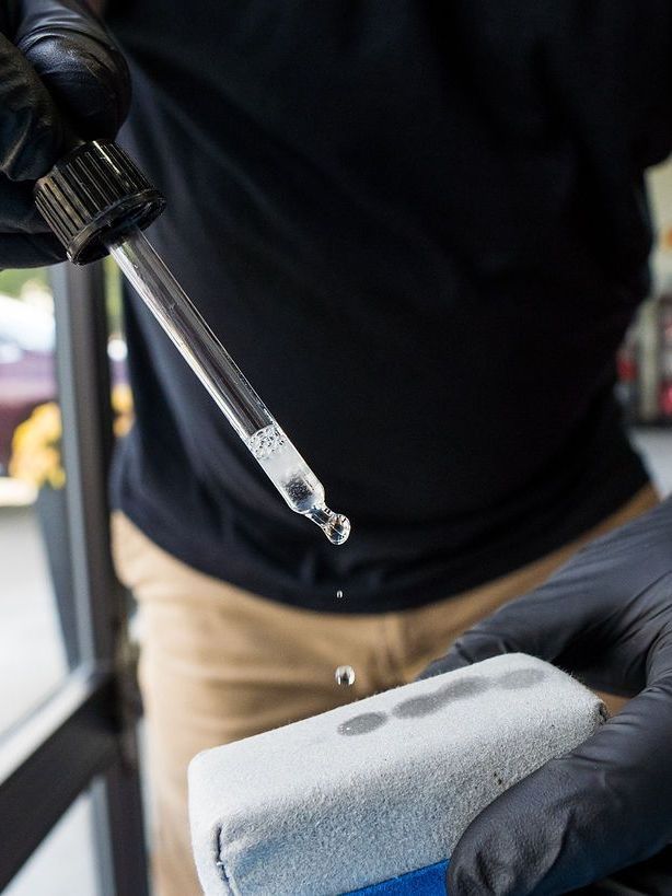 A person wearing black gloves is polishing a black car