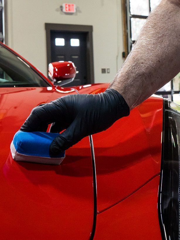 A person wearing black gloves is polishing a black car