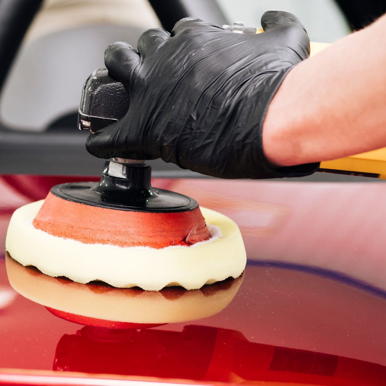 A person wearing black gloves is polishing a red car