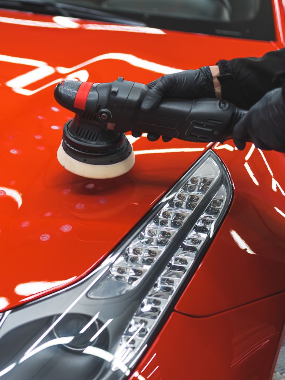 A person is polishing a red car with a machine.