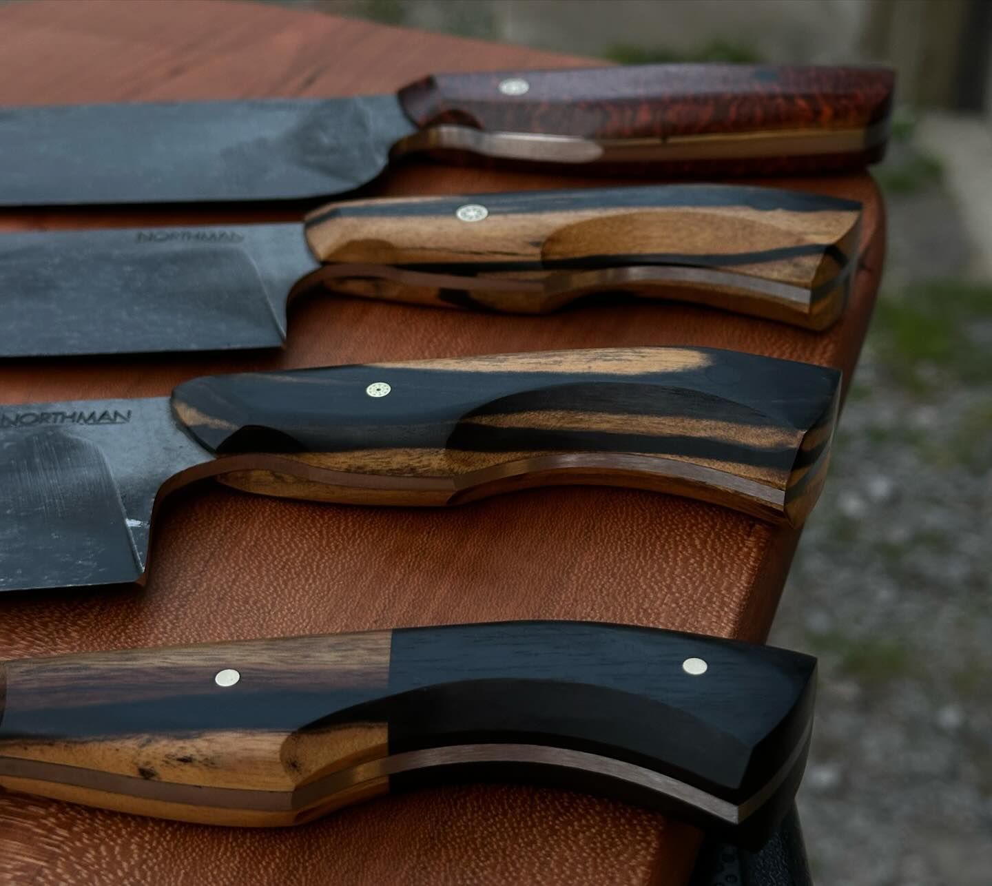 Close-up of four knives with wooden handles on a brown surface.