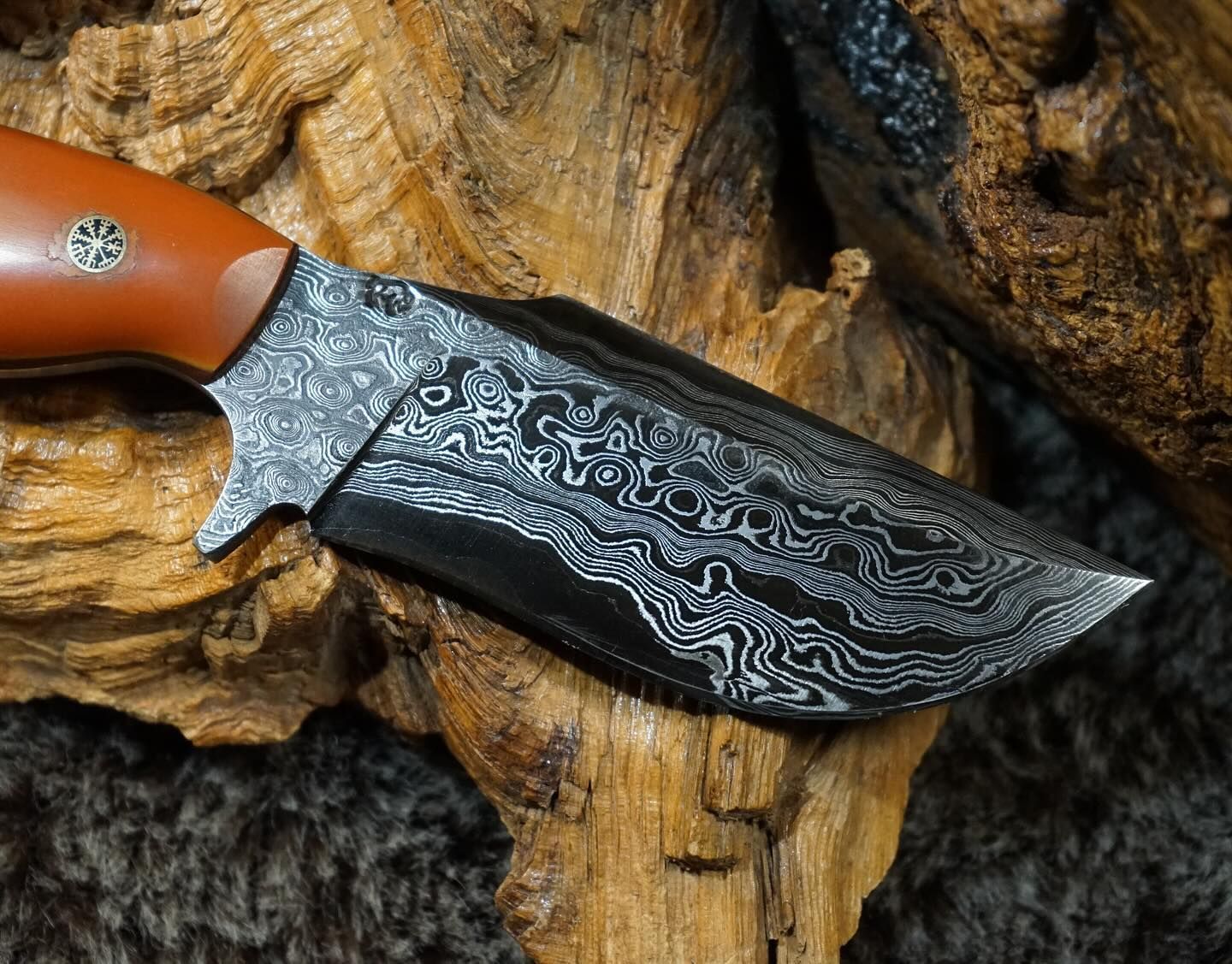 Damascus steel knife with brown handle, resting on textured wood.