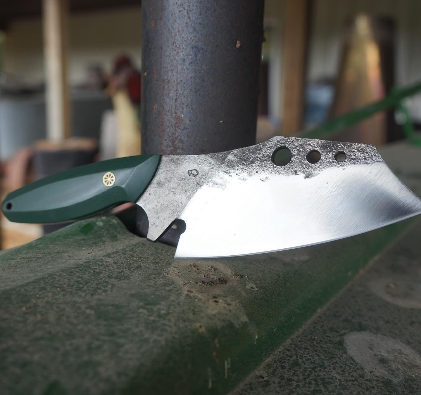Green-handled cleaver knife resting on a weathered green surface, with a dark background.