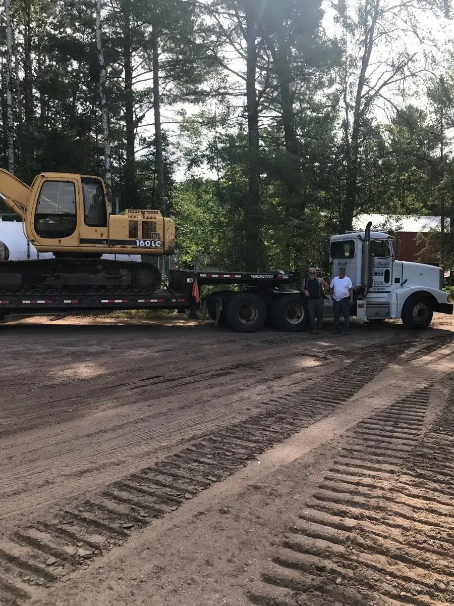 A yellow excavator is being towed by a white truck
