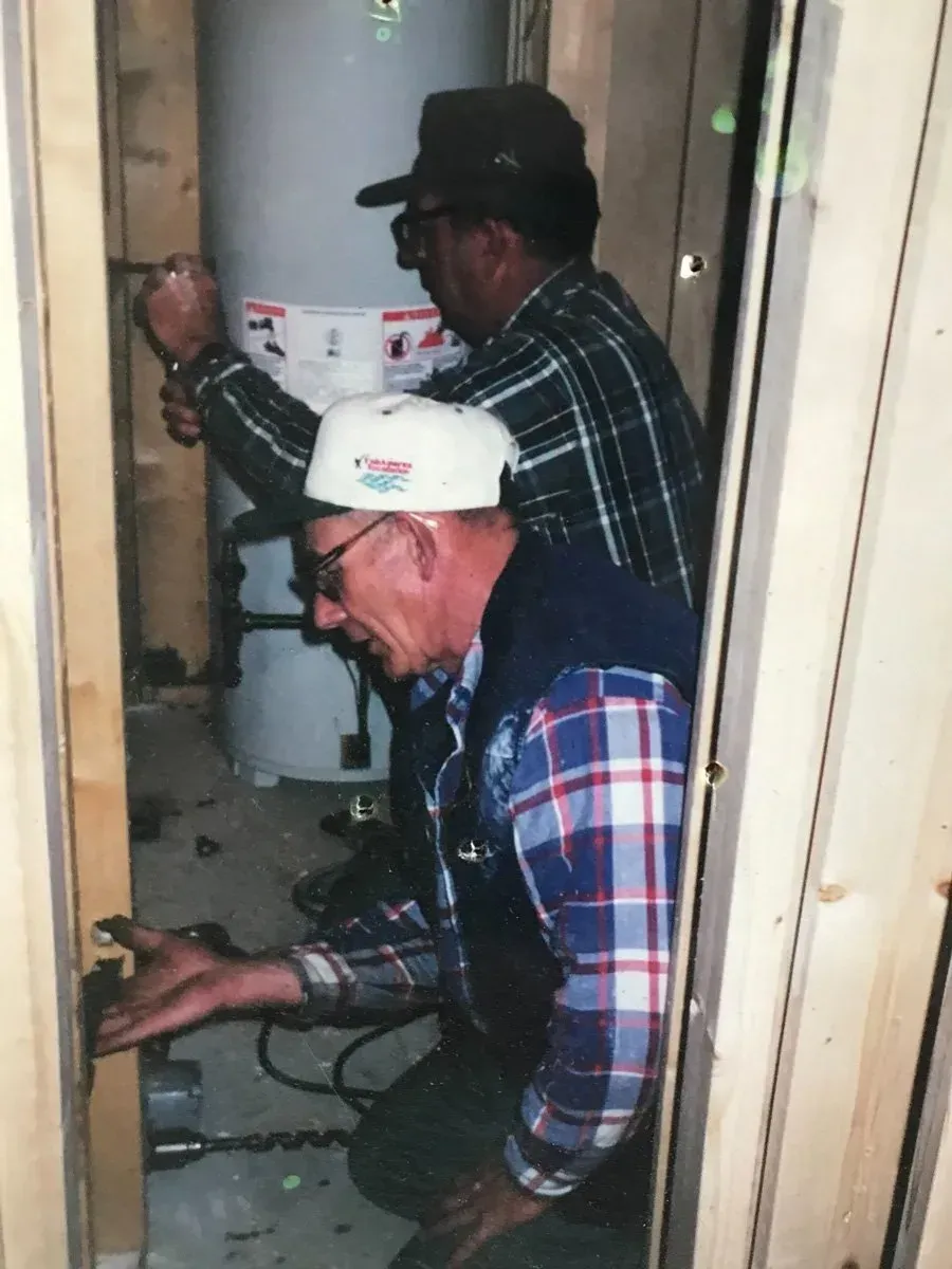 Two men are working on a water heater in a room