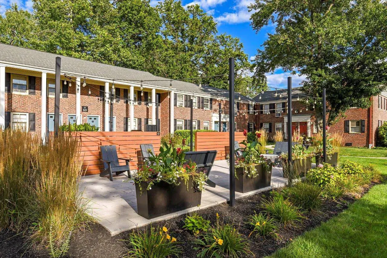 Outdoor community courtyard with string lights, planters, and seating in front of brick apartment buildings.