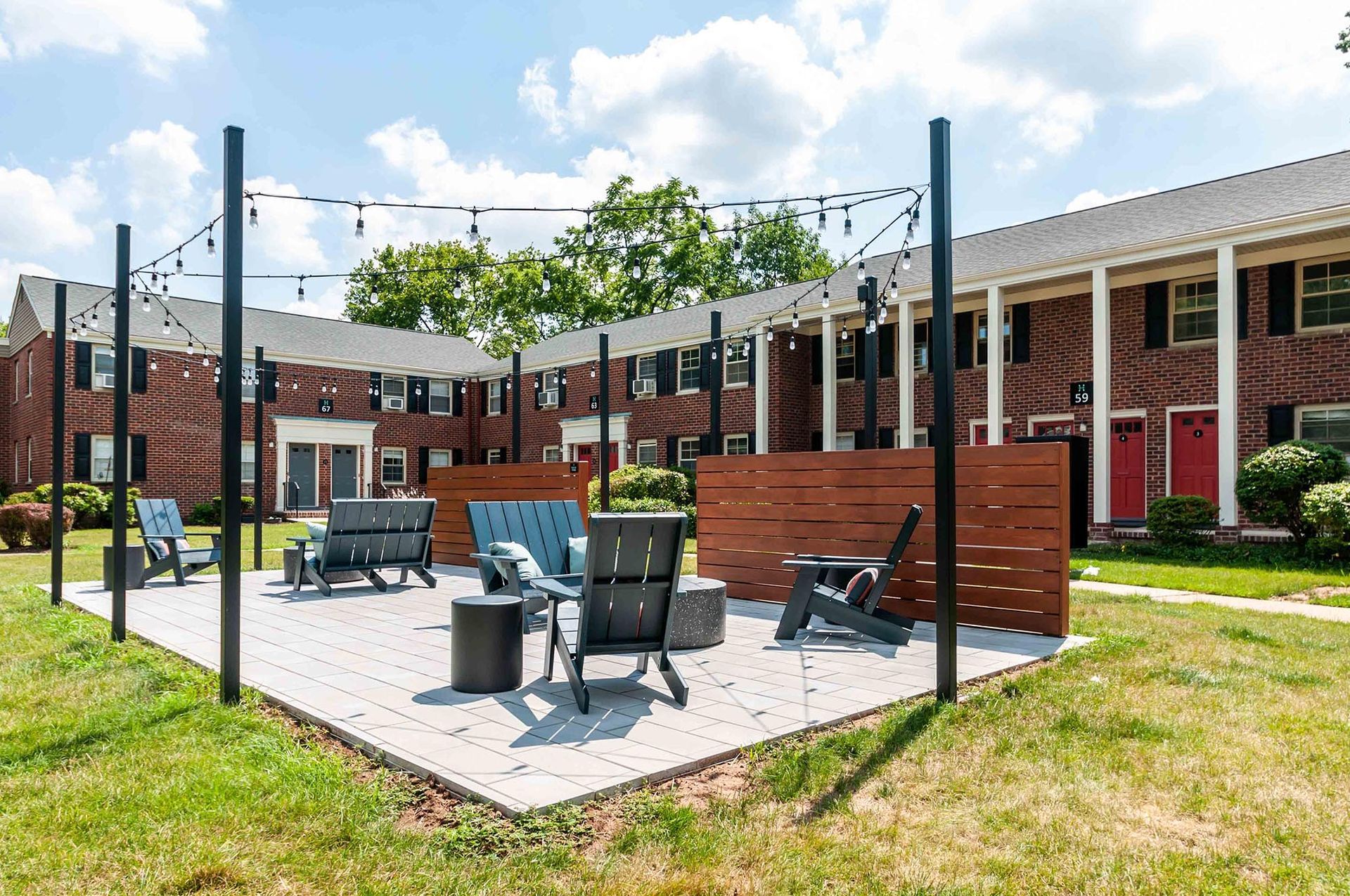Communal outdoor courtyard with string lights, seating, and privacy screens in a brick-apartment complex.