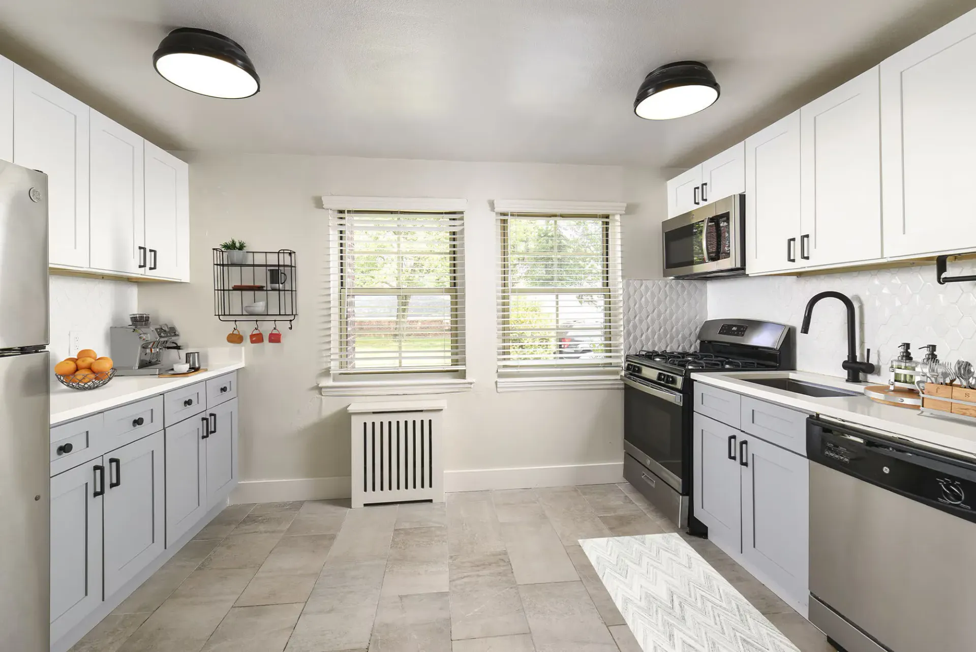 Bright, modern kitchen with white cabinets, stainless appliances, two windows, and tiled floor.