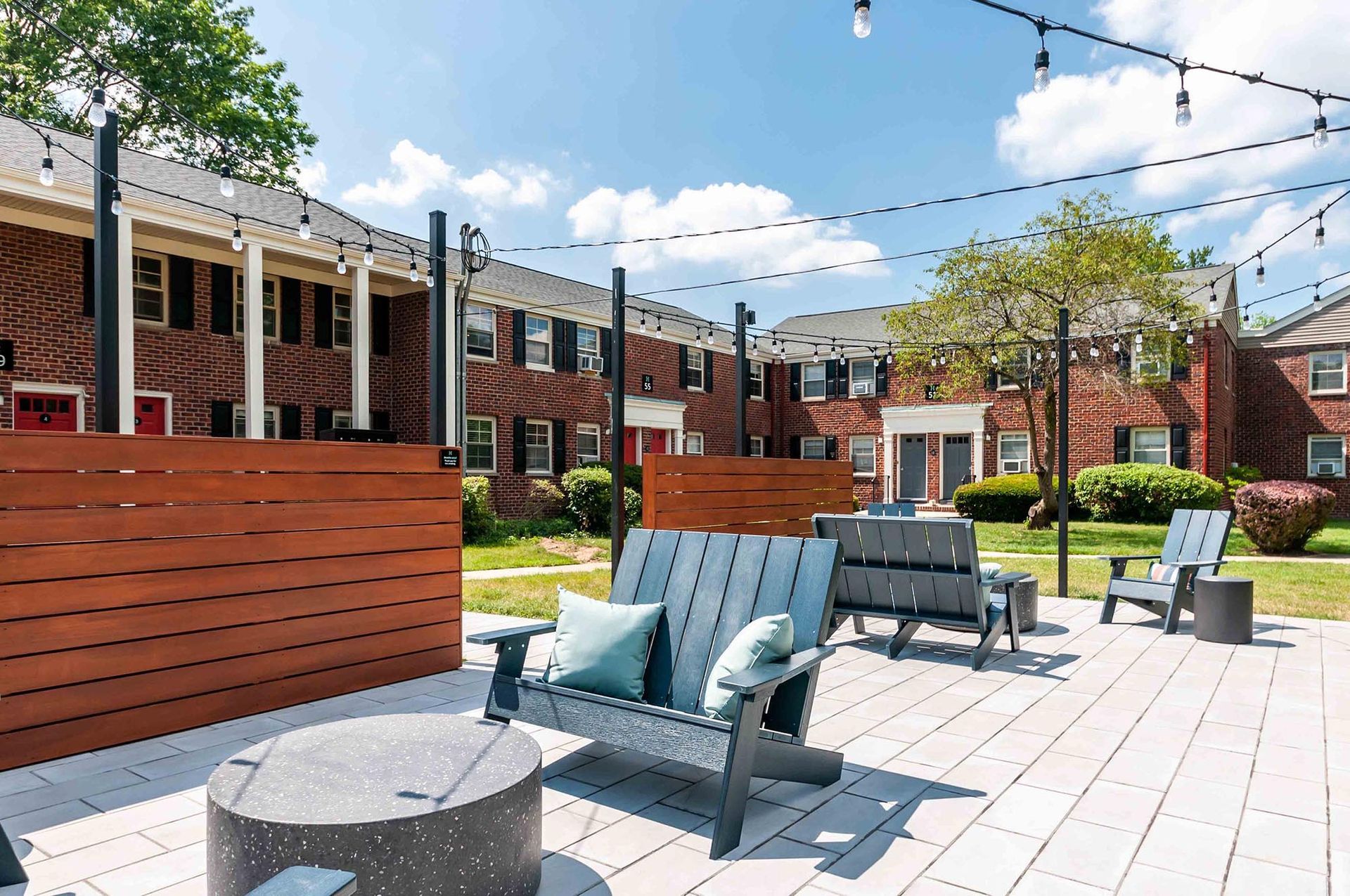 Outdoor communal courtyard with seating, string lights, and brick apartment buildings.