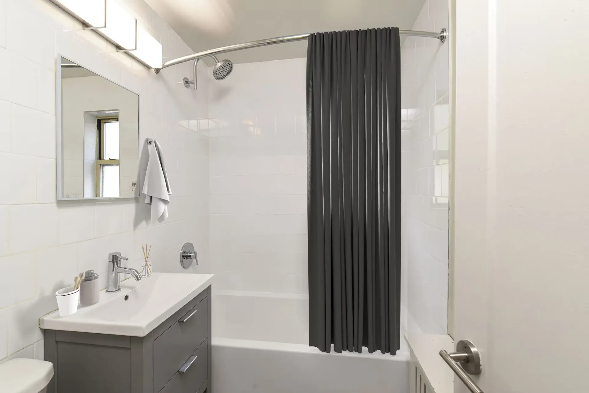 Bathroom with white tile walls, a gray vanity, mirror, and a curved shower curtain rod with a dark curtain.