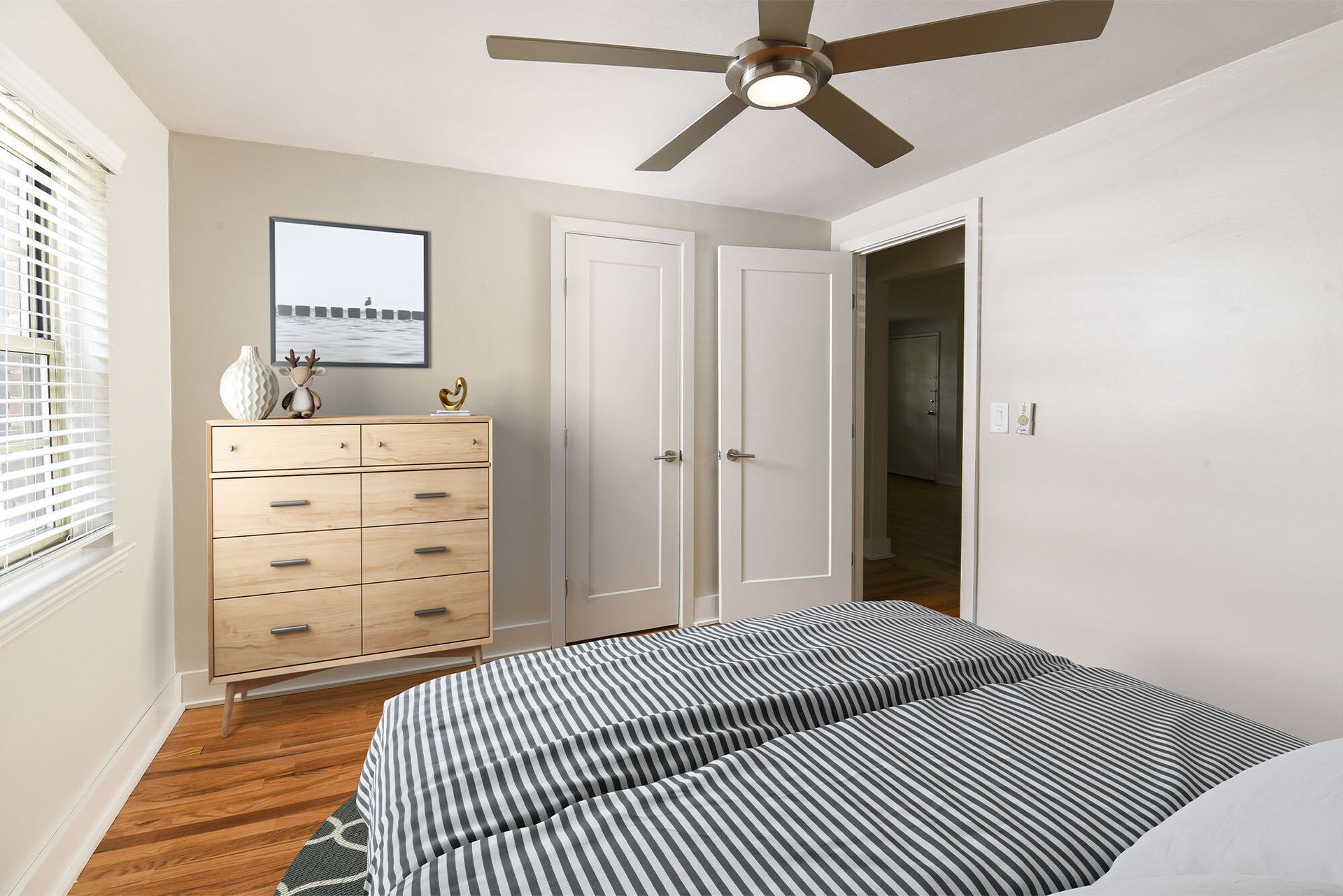 Bedroom with striped bedding, light wood dresser, ceiling fan, and open closet doors.