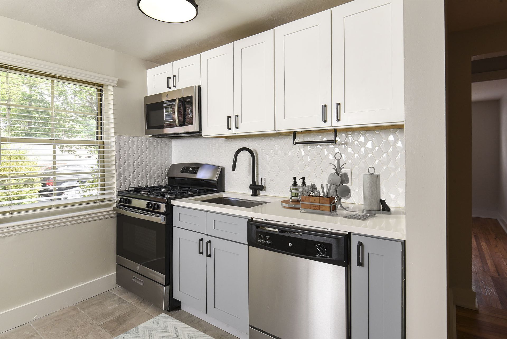 Bright apartment kitchen with white cabinets, stainless steel stove, microwave, and dishwasher.