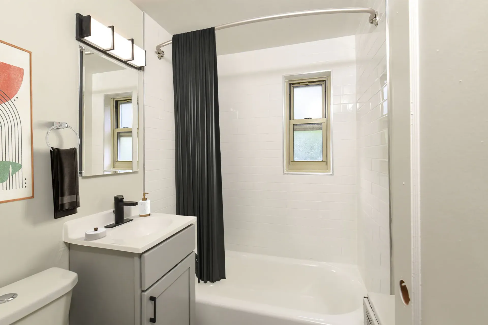 Bathroom with gray vanity, white sink, shower/tub with black curtain, white tiled walls, and a small window.