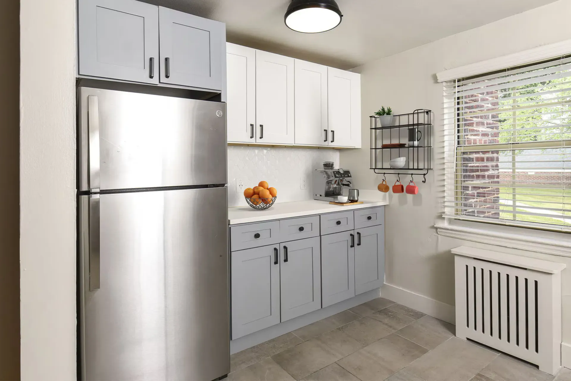 Kitchen in an apartment with stainless steel fridge, white upper cabinets, and gray lower cabinets.