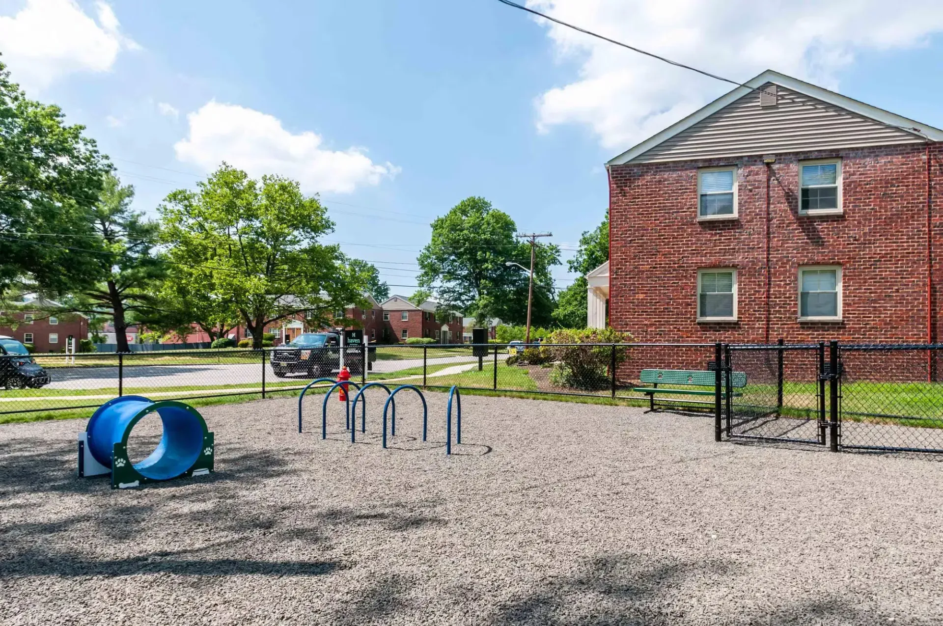 Outdoor community playground with a blue tunnel, arches, and a brick building behind a fence.