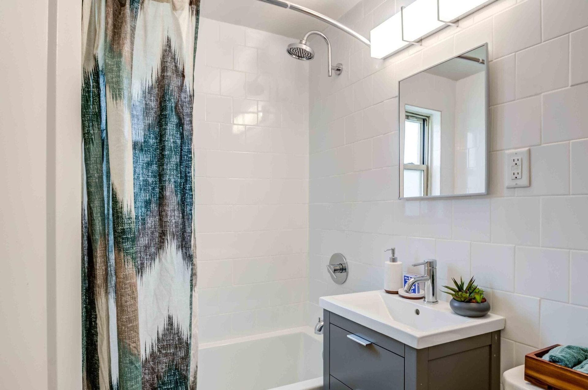 Bathroom with white tile walls, shower curtain, vanity, mirror, and a small plant.