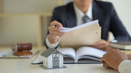 Modello di casa sulla scrivania durante una riunione di lavoro, con libro e documenti aperti.