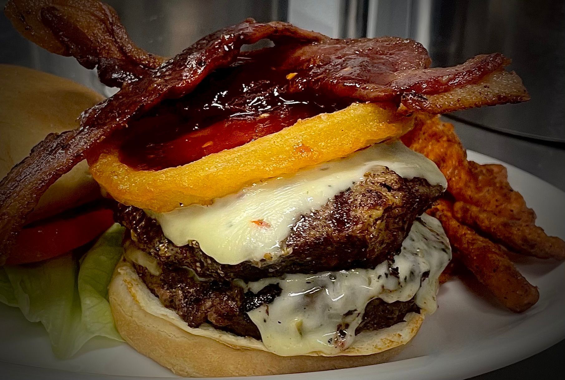 A close up of a hamburger with onion rings and bacon on a plate