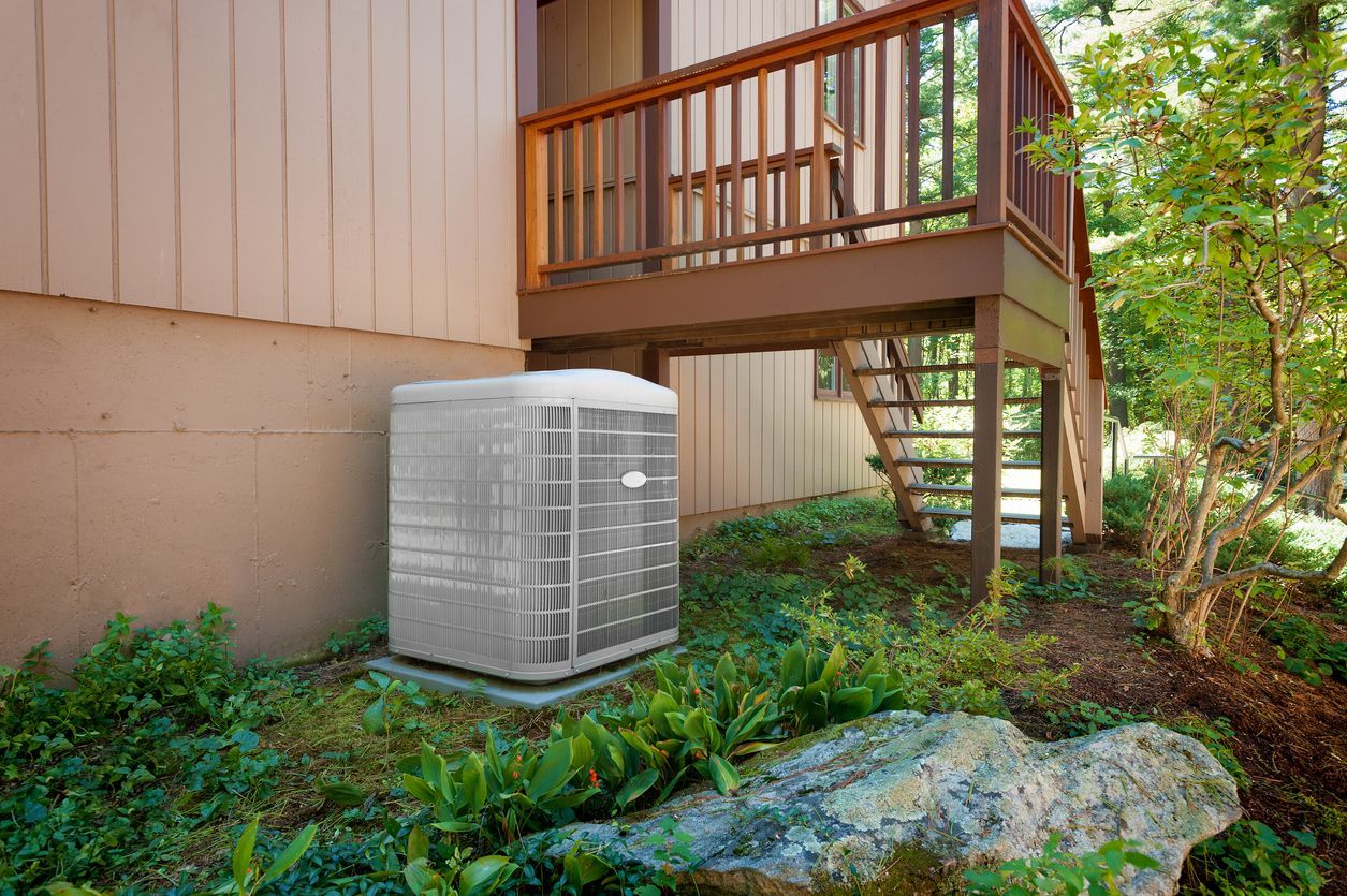 An air conditioner is sitting on the side of a house next to a deck.