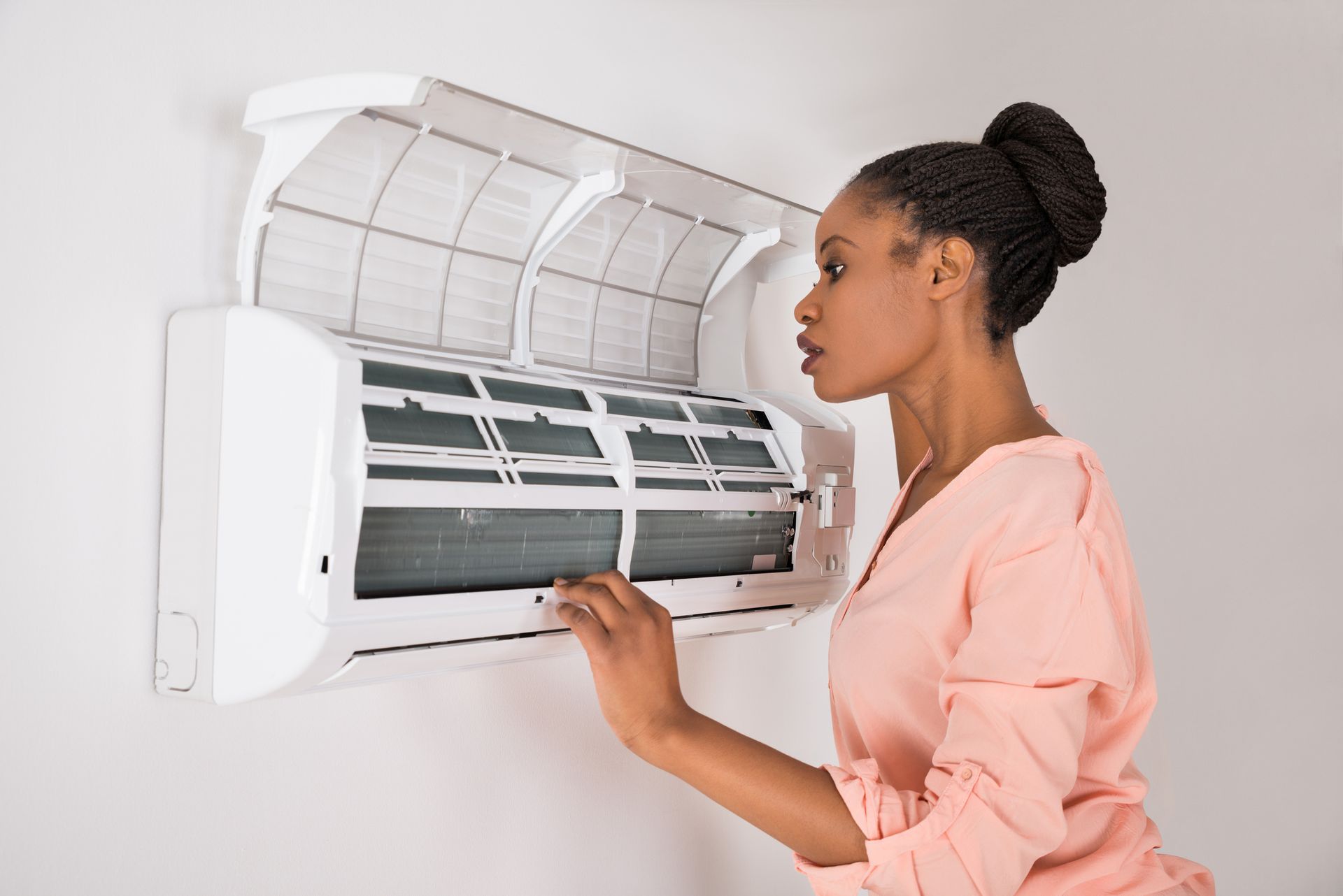 Woman checking air conditioning at home for repairs.