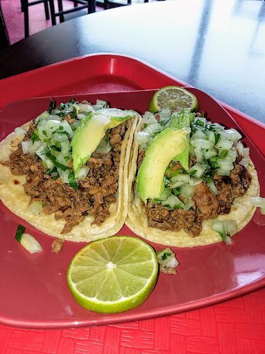 Two tacos with avocado and lime on a red plate on a tray.