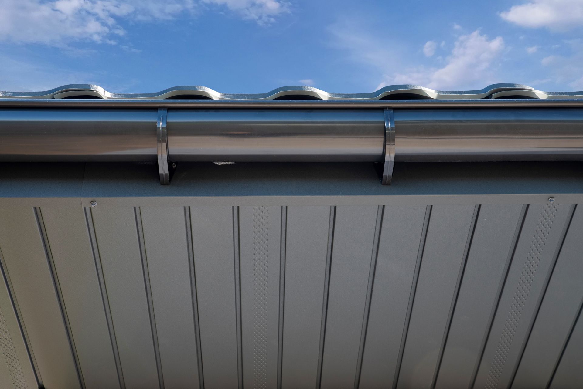 Close-up of a building roof edge with gray siding and blue sky above Close-up of a building roof edge with gray siding and blue sky above