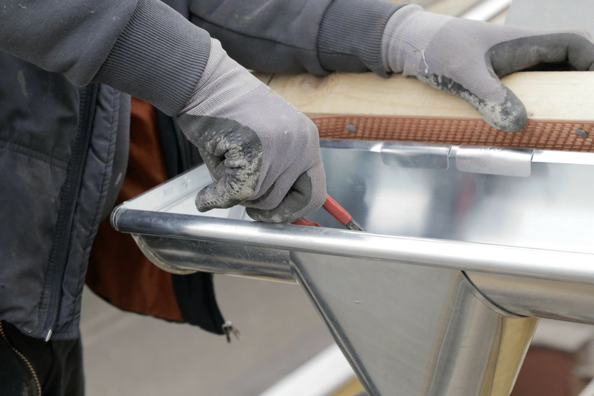 Gloved hands using a red scraper on a metal tray outdoors