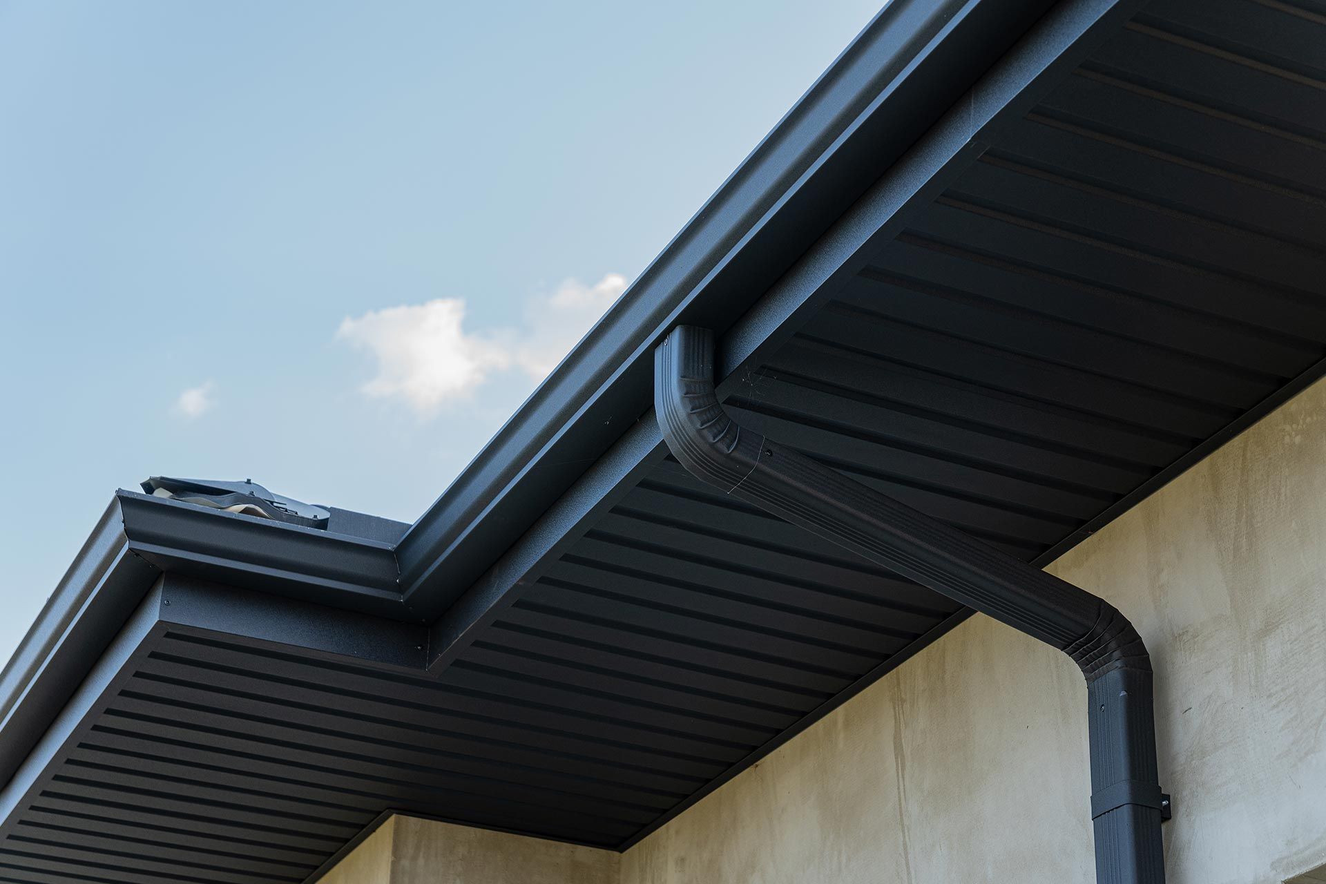 Close-up of a house roofline with dark gutters and soffit against a blue sky Close-up of a house roofline with dark gutters and soffit against a blue sky