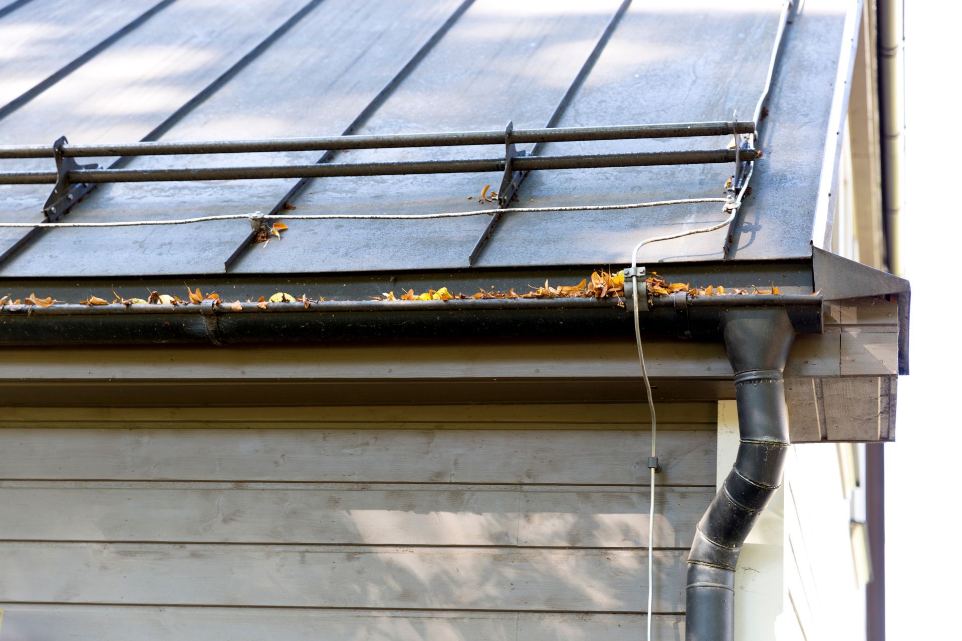 Gutter and downspout on a house roof with rainwater dripping over the edge Gutter and downspout on a house roof with rainwater dripping over the edge