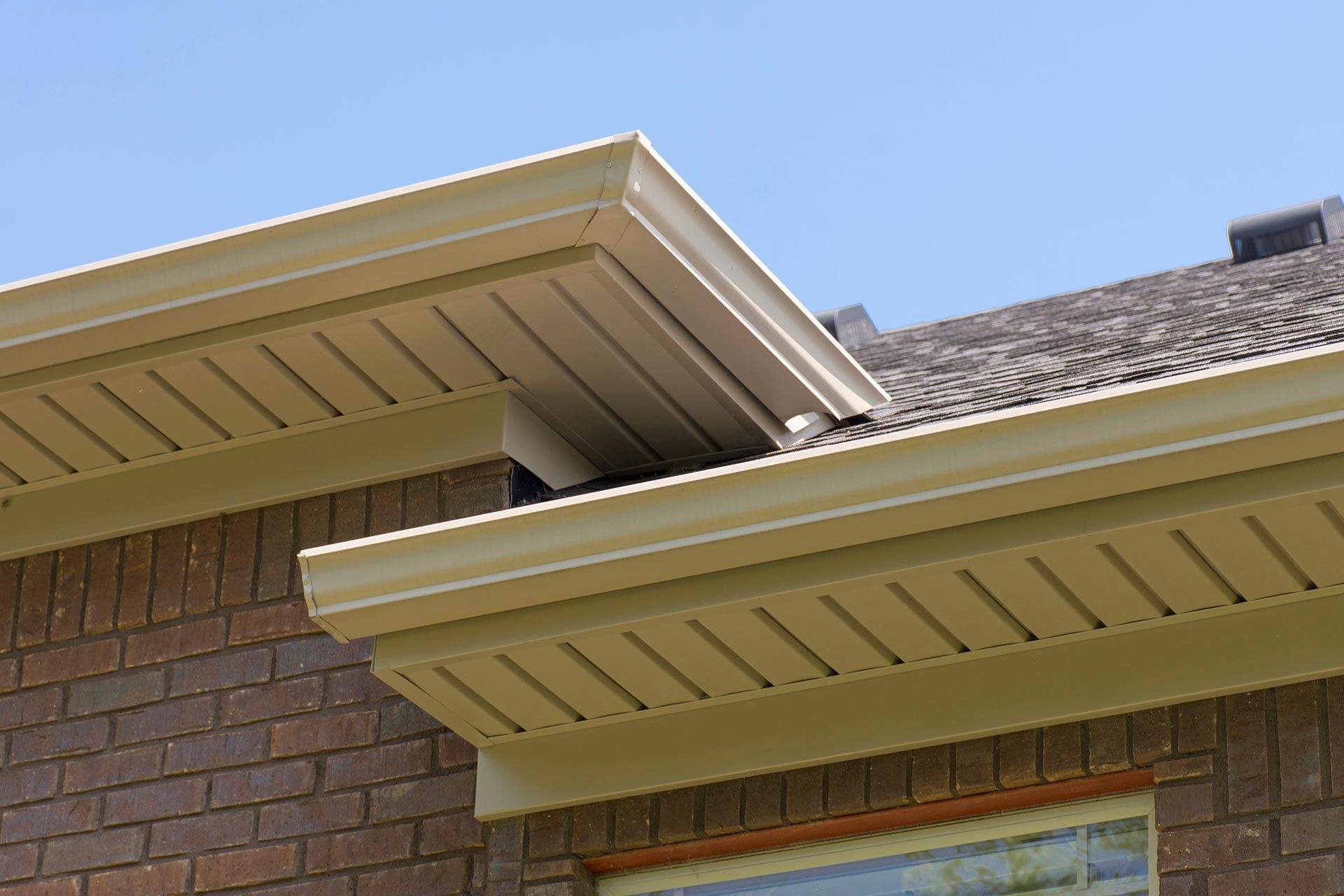 Close-up of a brick house roof with beige eaves and gutters against a blue sky Close-up of a brick house roof with beige eaves and gutters against a blue sky