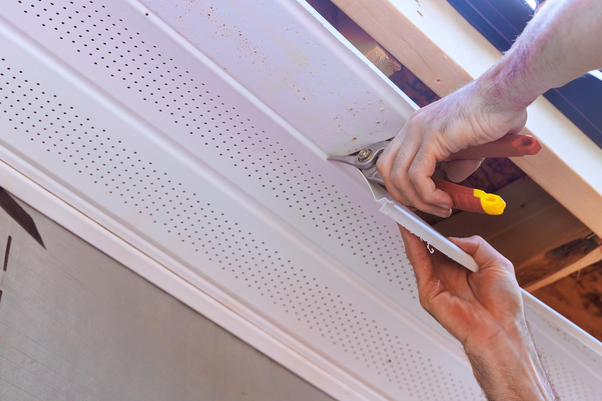 Hands using a screwdriver to install a white perforated ceiling panel near exposed wooden beams