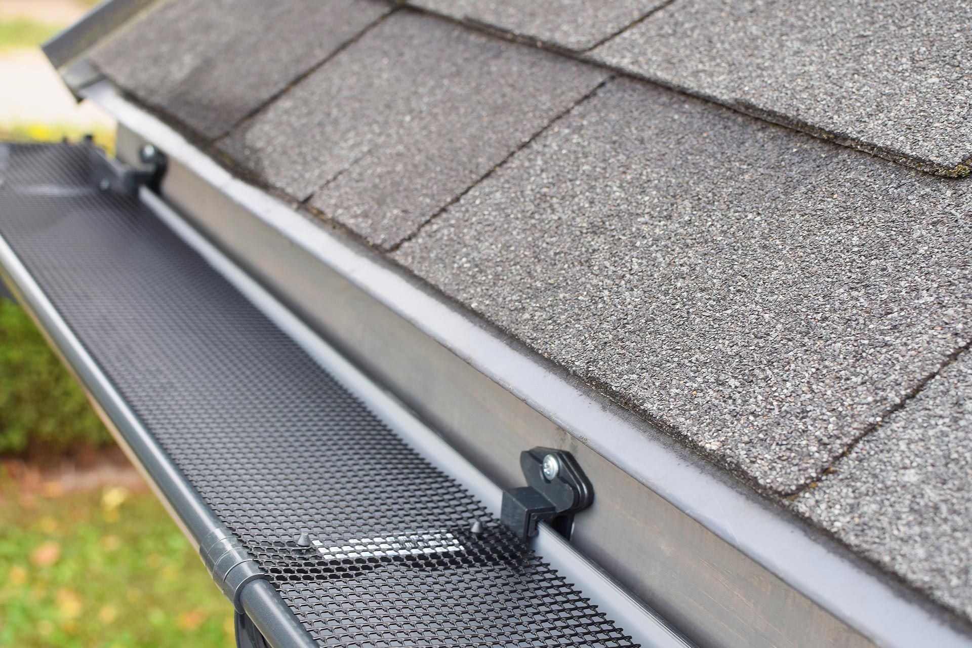 Gutter guard along a gray shingled roof edge beside a downspout outlet
