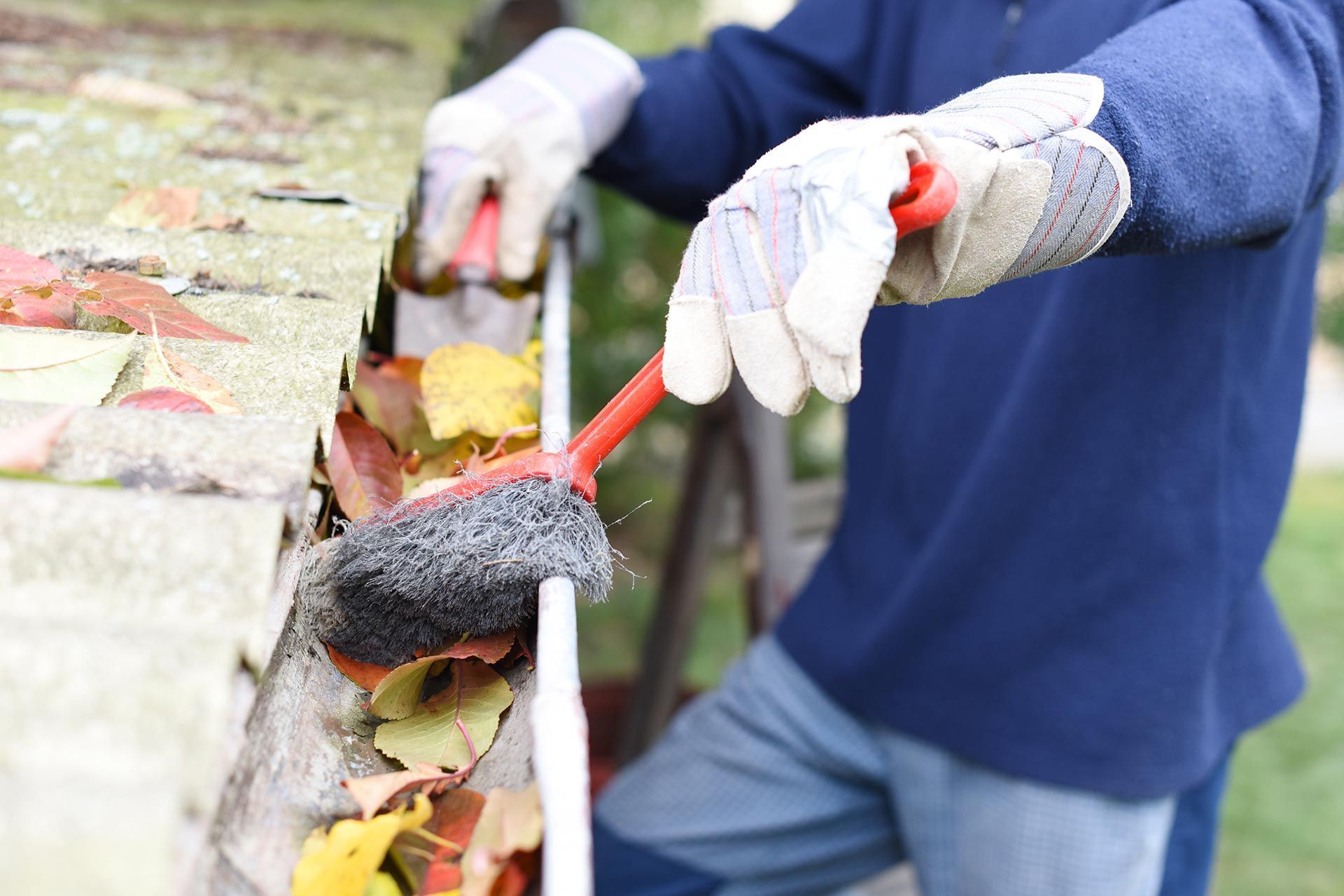 Gloved hands cleaning a leaf-filled gutter with a brush outdoors Gloved hands cleaning a leaf-filled gutter with a brush outdoors