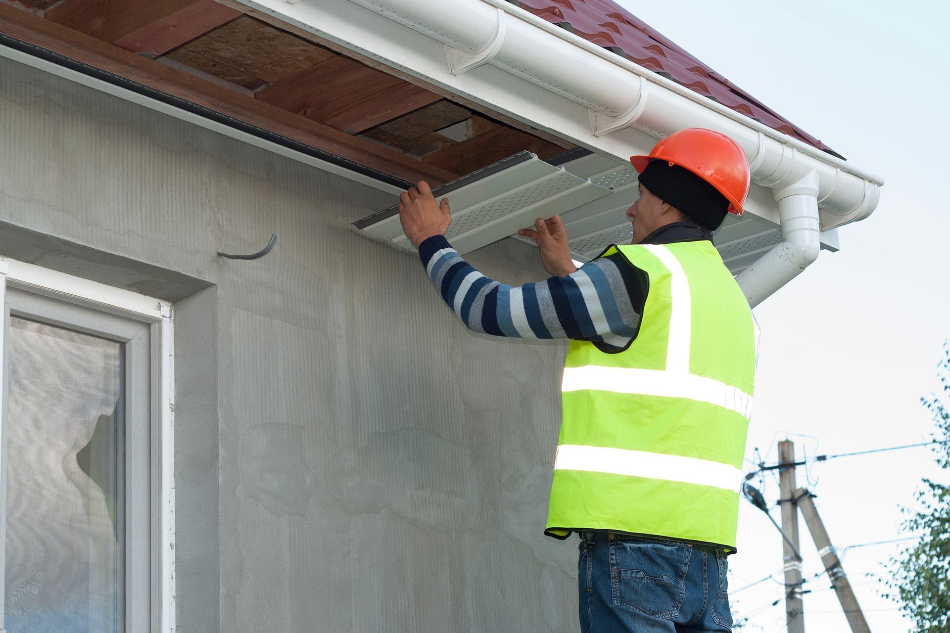 Worker in orange hard hat and safety vest repairing a roof gutter on a house