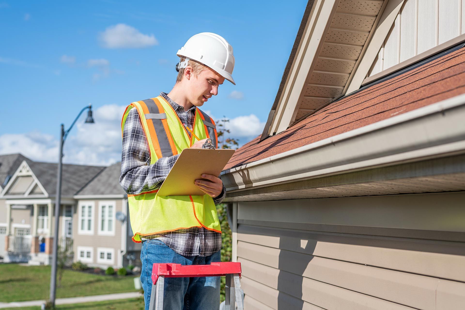 Construction worker inspecting a house roof with a clipboard and hard hat Construction worker inspecting a house roof with a clipboard and hard hat