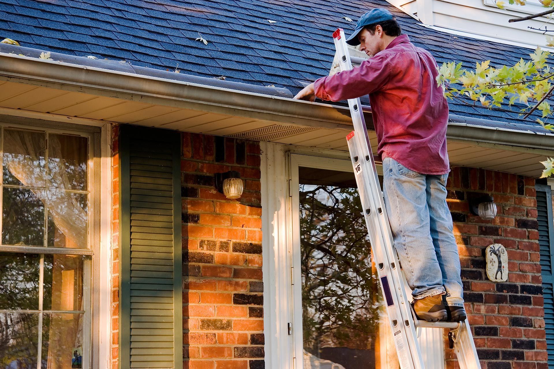 Worker on a ladder repairing a roof edge on a brick house Worker on a ladder repairing a roof edge on a brick house