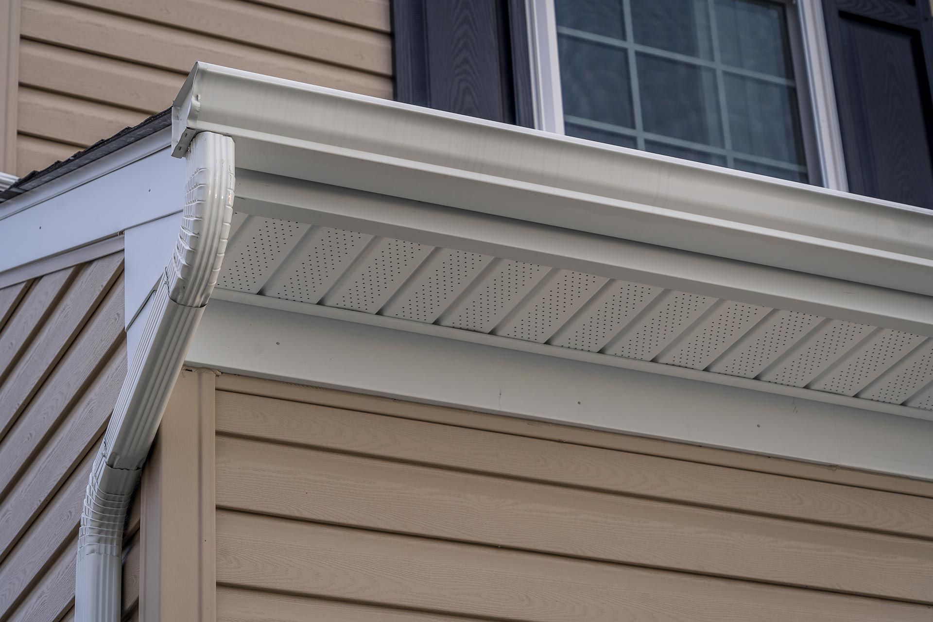 Close-up of white gutter and soffit on beige house exterior with window above Close-up of white gutter and soffit on beige house exterior with window above