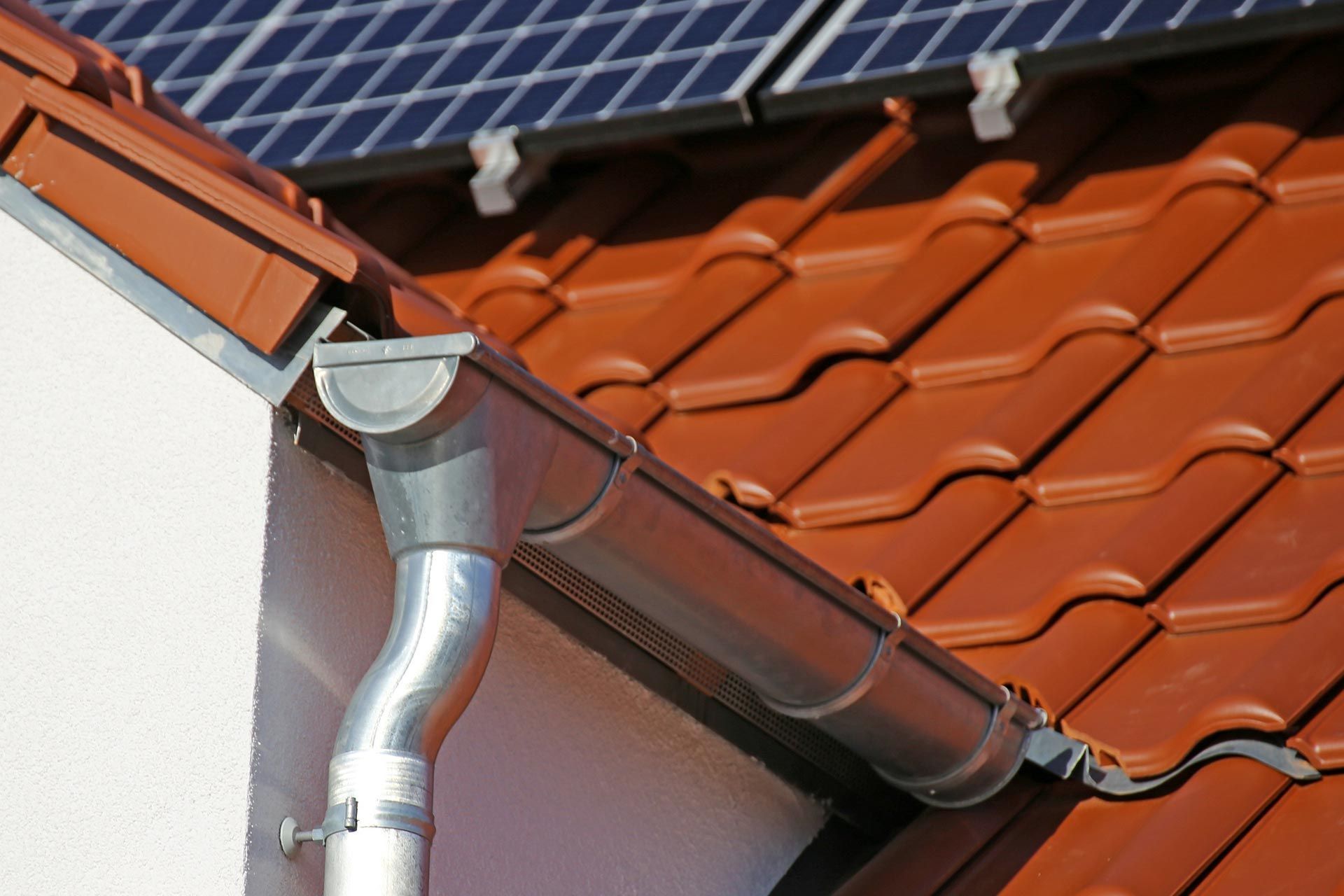 Metal gutter and downspout on a red tile roof beside solar panels Metal gutter and downspout on a red tile roof beside solar panels