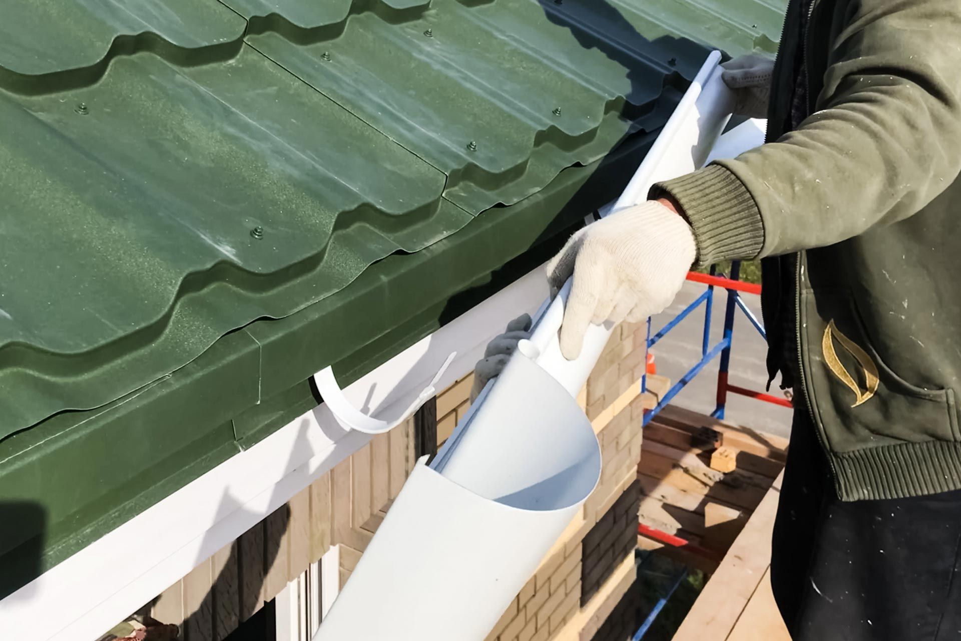 Person in gloves pouring white sealant along the edge of a green metal roof