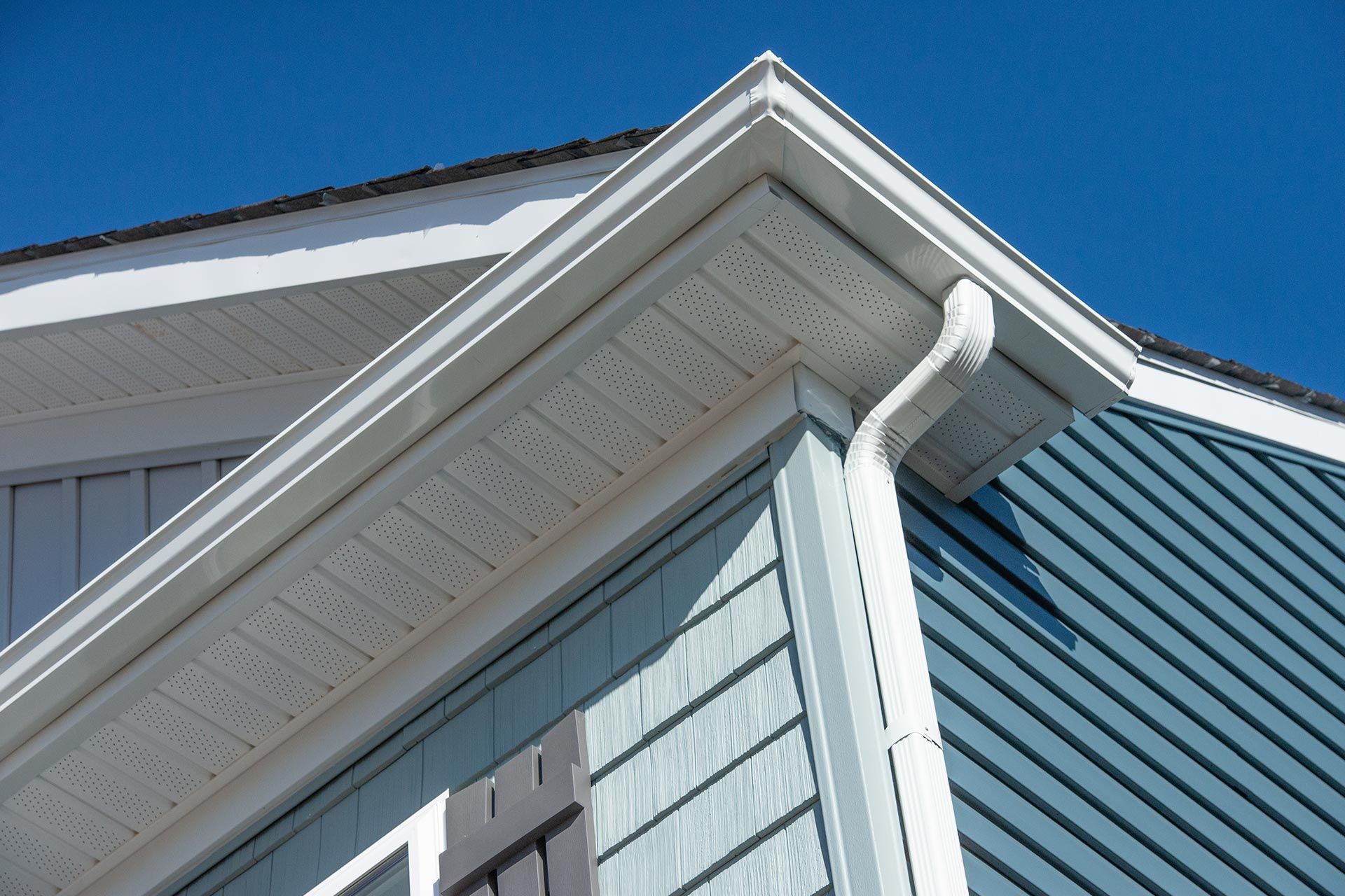 White house roof and blue siding with a gutter under a clear blue sky White house roof and blue siding with a gutter under a clear blue sky
