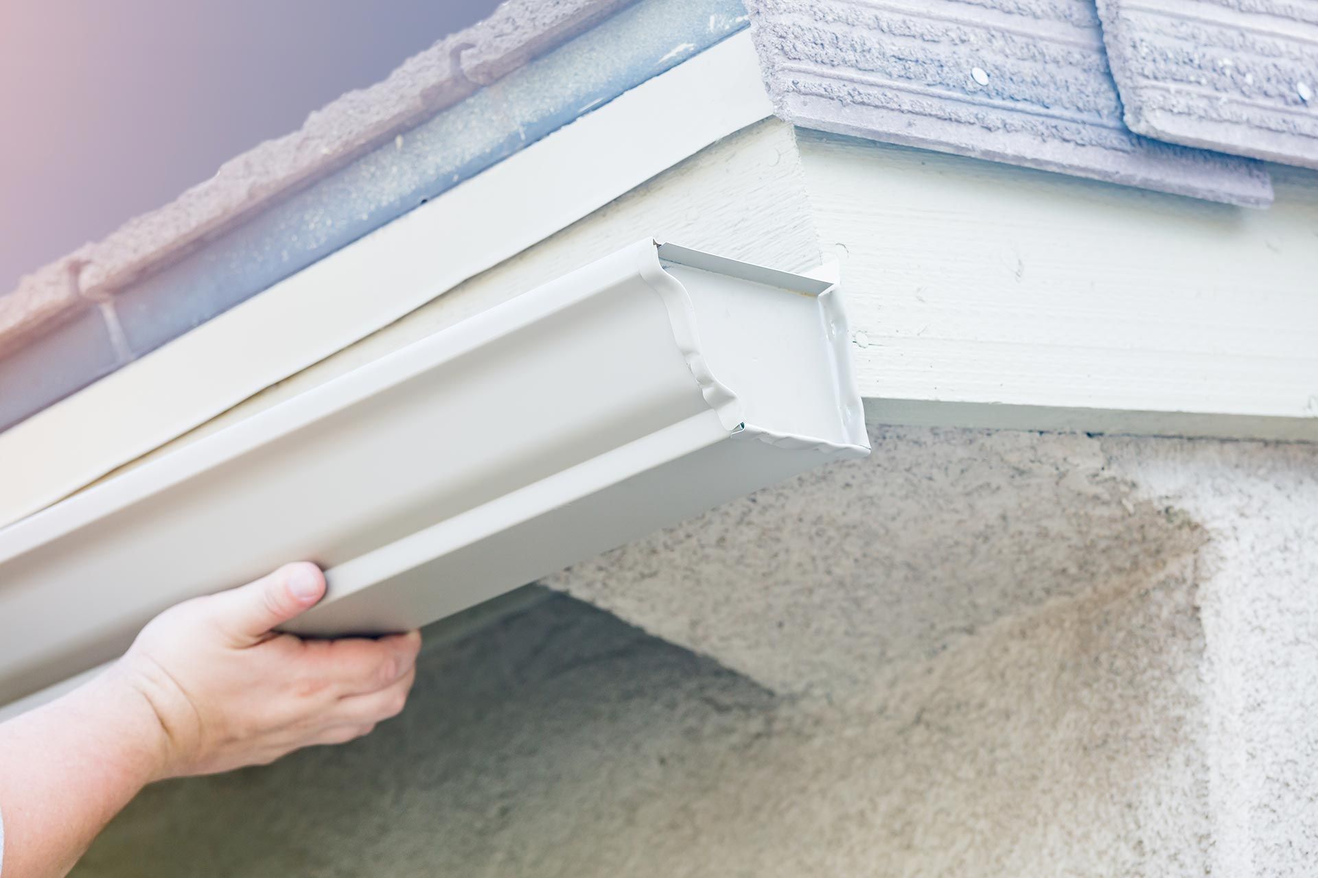 Hand lifting a white gutter attached to a house roofline Hand lifting a white gutter attached to a house roofline
