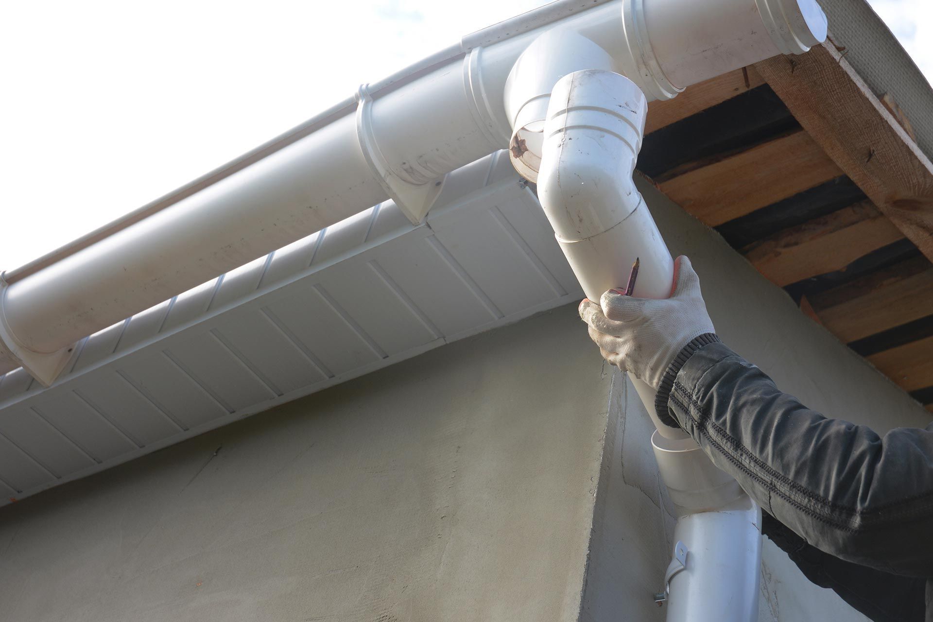 Person installing white gutter downspout on a roof edge with a gloved hand
