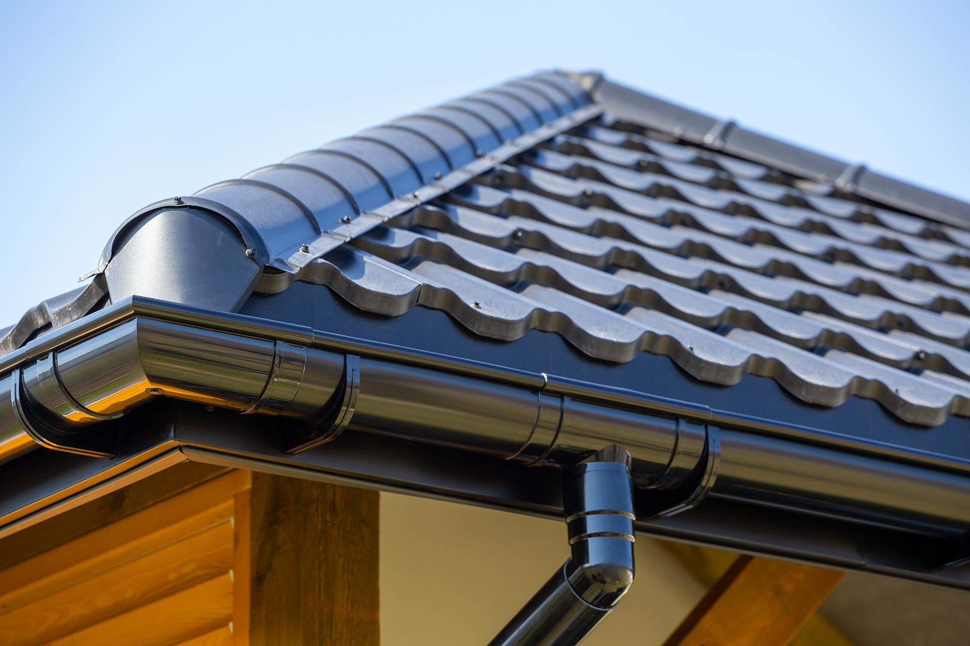 Black gutter and downspout on a tiled house roof under a blue sky Black gutter and downspout on a tiled house roof under a blue sky